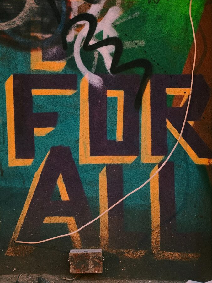 Decorative image of a graffiti wall that says FOR ALL in black lettering with orange outline